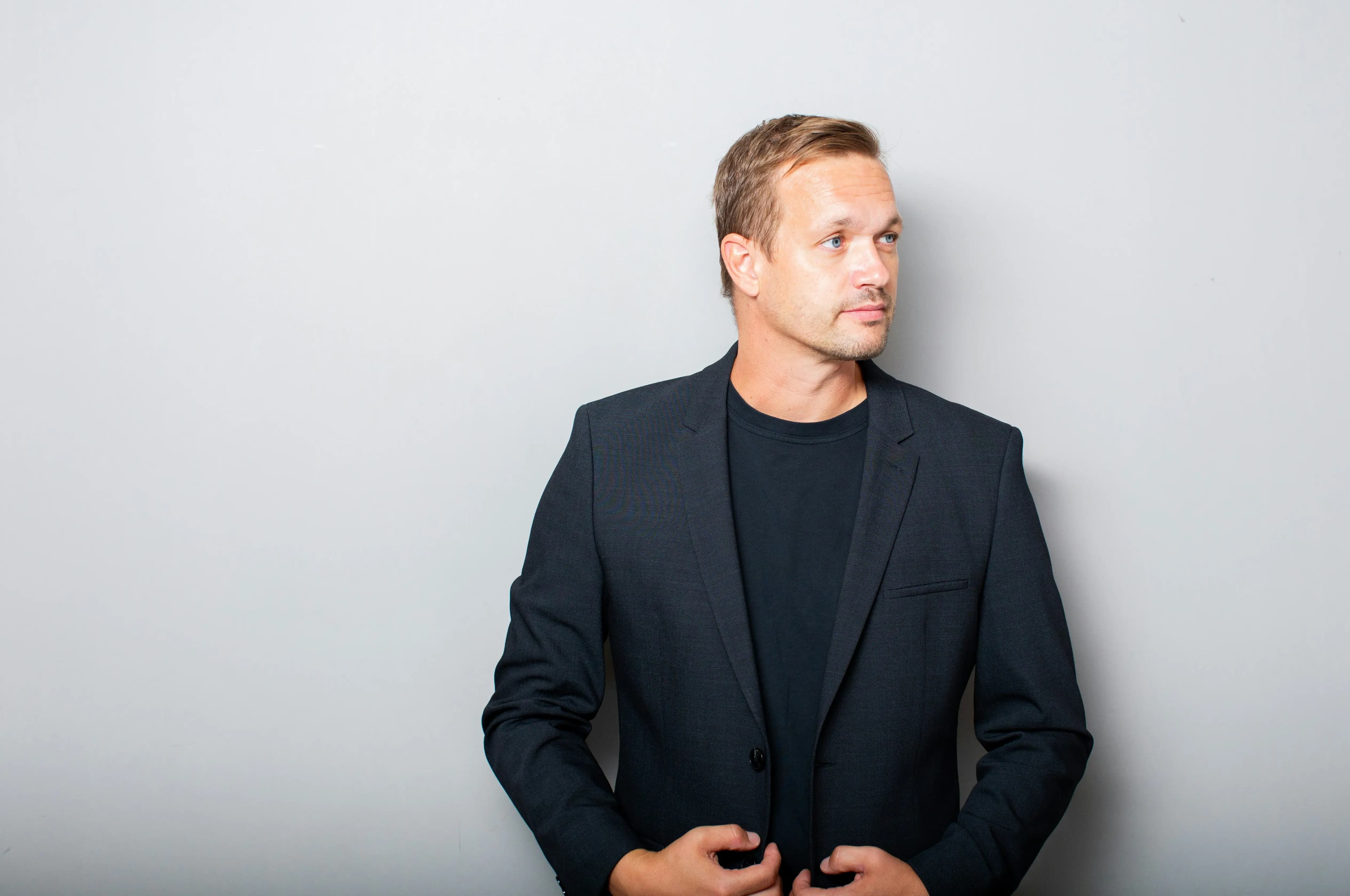 Confident man in a dark blazer against a gray background, representing improved energy, muscle mass, and vitality through Mind & Body Infusions' testosterone replacement therapy